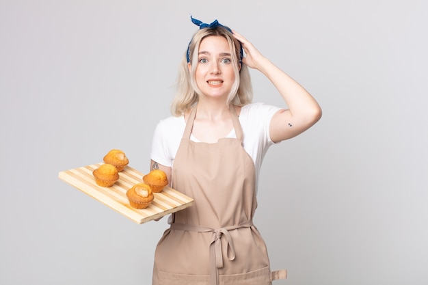 young pretty albino woman feeling stressed, anxious or scared, with hands on head with a muffins tray