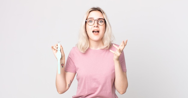 Photo young pretty albino woman looking desperate, frustrated and stressed holding a watch clock