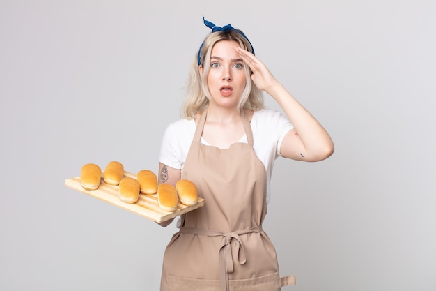 Young pretty albino woman looking happy, astonished and surprised with a bread buns tray