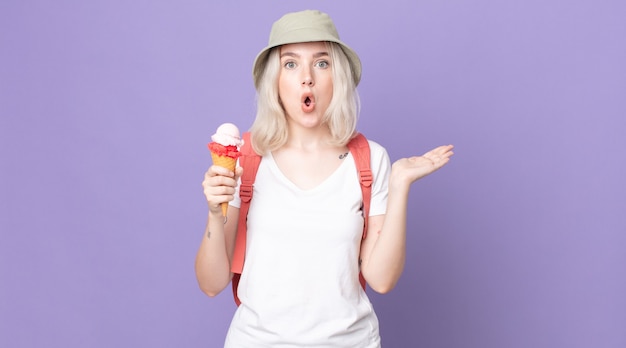 Young pretty albino woman looking surprised and shocked, with jaw dropped holding an object .summer concept