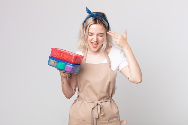 Young pretty albino woman looking unhappy and stressed, suicide gesture making gun sign holding food tupperwares