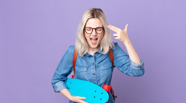 Young pretty albino woman looking unhappy and stressed, suicide gesture making gun signand holding a skateboard