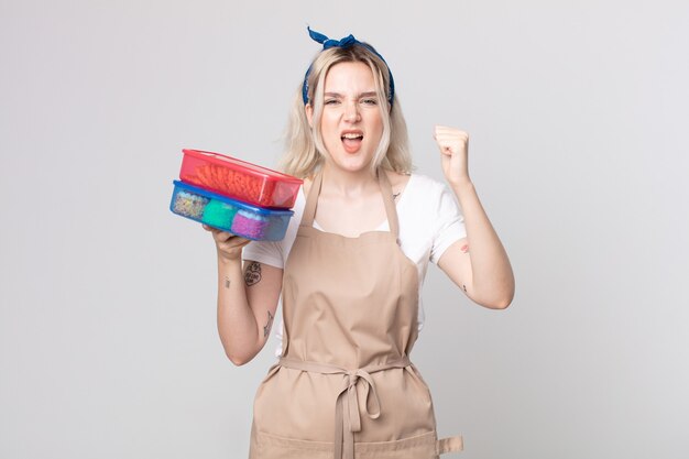 young pretty albino woman shouting aggressively with an angry expression holding food tupperwares