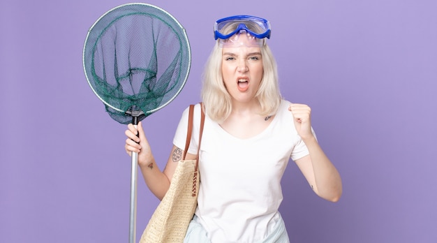 Young pretty albino woman shouting aggressively with an angry expression with goggles and a fishing net