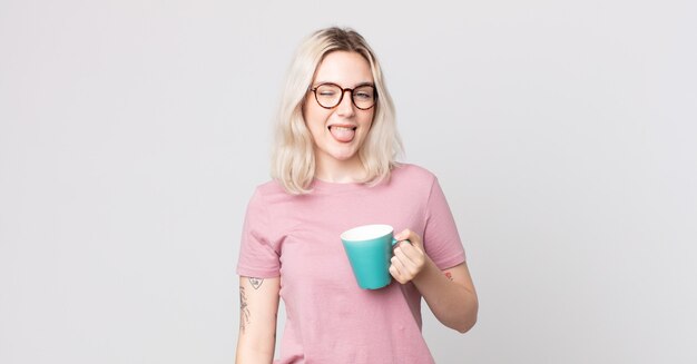 Young pretty albino woman with cheerful and rebellious attitude, joking and sticking tongue out with a coffee mug