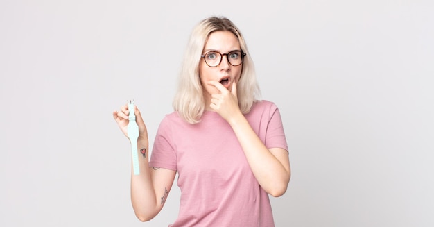 young pretty albino woman with mouth and eyes wide open and hand on chin holding a watch clock