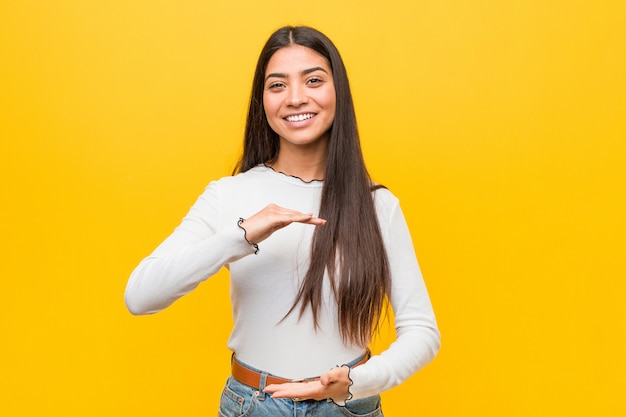 Young pretty arab woman against a yellow background holding something with both hands, product presentation.