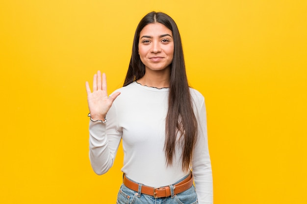 Young pretty arab woman against yellow  smiling cheerful showing number five with fingers.