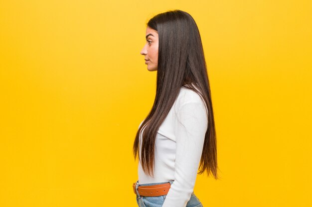 Young pretty arab woman against a yellow wall gazing left, sideways pose.