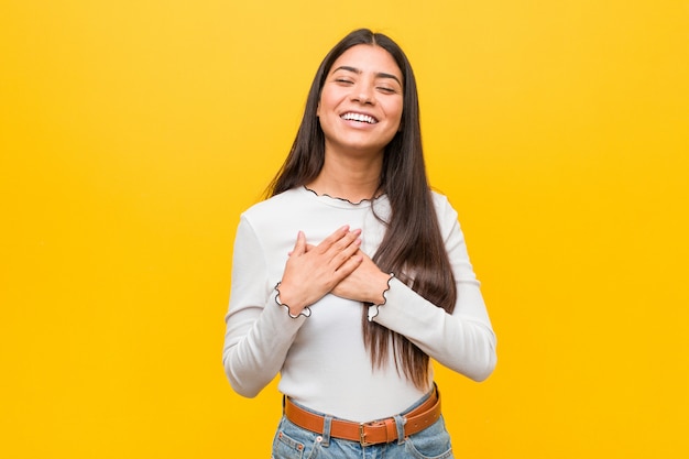 Young pretty arab woman against a yellow wall laughing keeping hands on heart, concept of happiness