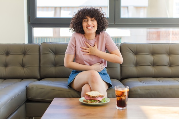 Фото Молодая красивая арабская женщина ест бутерброд, сидя на диване у себя дома
