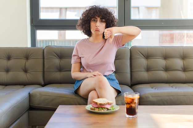 Молодая красивая арабская женщина ест бутерброд, сидя на диване у себя дома
