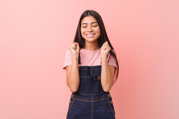 Young pretty arabic  woman wearing a jeans dungaree raising fist, feeling happy and successful. Victory concept.