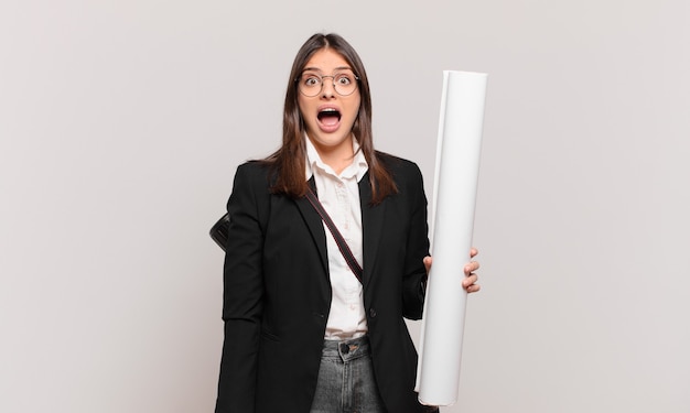 Young pretty architect woman looking very shocked or surprised, staring with open mouth saying wow