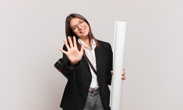 Young pretty architect woman smiling and looking friendly, showing number five or fifth with hand forward, counting down