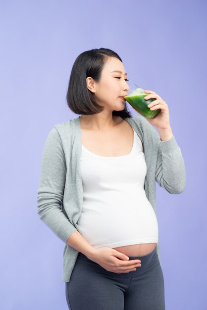 Young pretty Asian pregnant woman drinking green juice