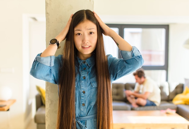 Giovane donna abbastanza asiatica che si sente stressata, preoccupata, ansiosa o spaventata, con le mani sulla testa, in preda al panico per errore