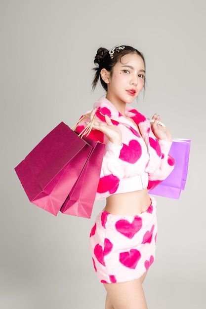 Young Pretty Asian woman have prefect slim fit body in heart print dress with makeup on face holding colorful shopping bags isolated on white background Valentine love plastic surgery concept