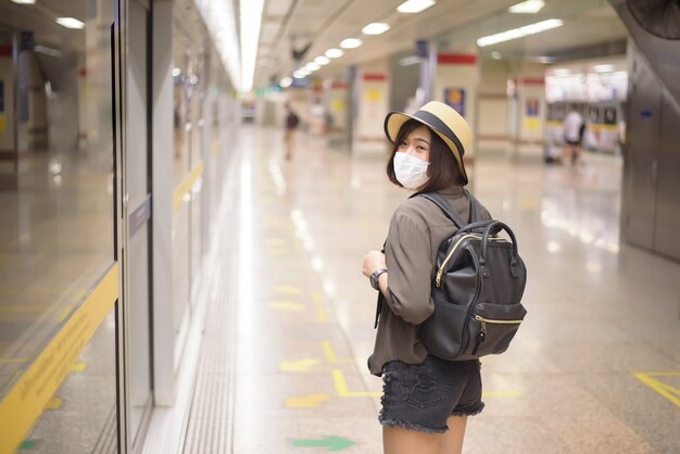 A young pretty Asian woman is wearing protective mask standing in metro station