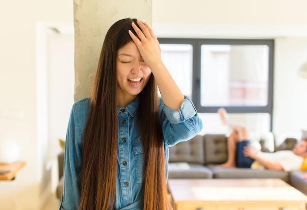 Young pretty asian woman laughing and slapping forehead