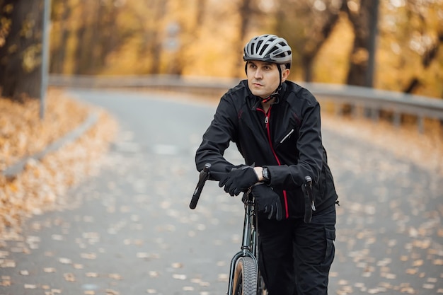 Young pretty athletic man standing with bicycle in autumn park