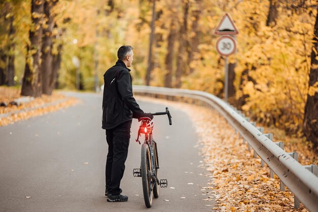Молодой красивый спортивный мужчина стоит с велосипедом в осеннем парке