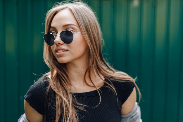 Photo young pretty attractive girl in denim clothes in glasses on a simple dark green background with place for text.