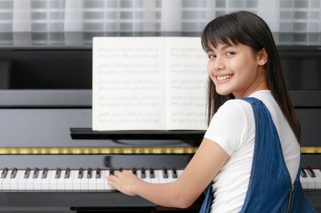 ぼやけた楽譜とメトロノーム、リズム機器でピアノに座っている若いかなり美しいアジアの女の子
