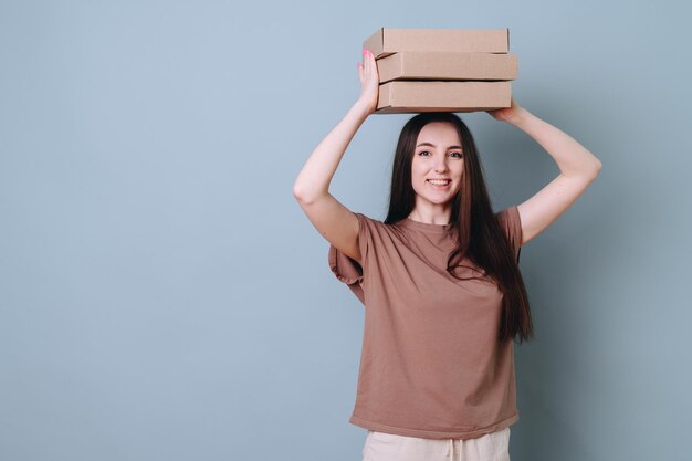 Young pretty beautiful smiling woman holding over her head a stack of boxes as a joke