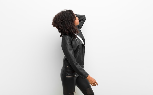 Giovane donna di colore graziosa che indossa una giacca di pelle contro il muro bianco