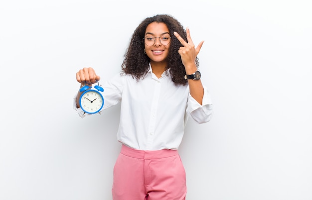 Photo young pretty black woman with an alarm clock against white wall