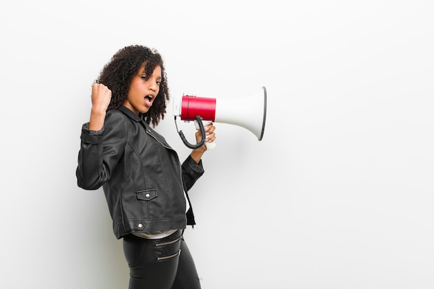 Young pretty black woman with a megaphone wearing a leather jacket against white wall