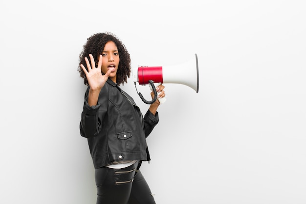 Young pretty black woman with a megaphone wearing a leather jacket against white 