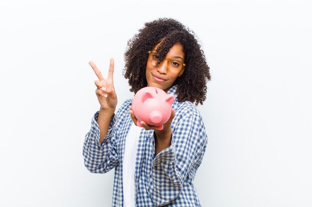 Young pretty black woman with a piggy bank against white 