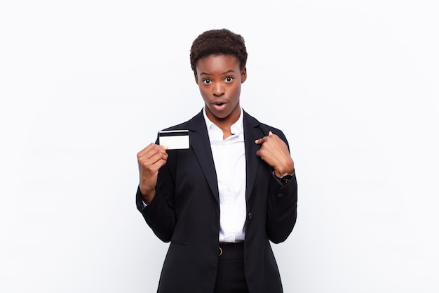 Young pretty black womanfeeling happy, surprised and proud, pointing to self with an excited, amazed look holding a credit card