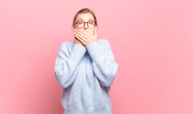 Young pretty blond woman covering mouth with hands with a shocked, surprised expression, keeping a secret or saying oops