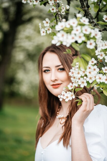 Young pretty blond woman smelling flowers in blooming sakura garden.