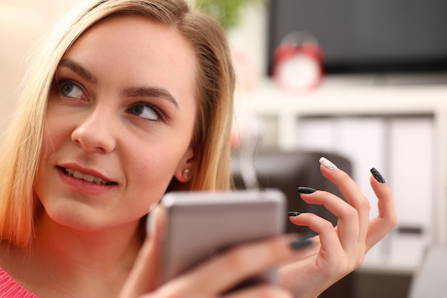 Young pretty blond womansit on sofa hold smartphone in hands