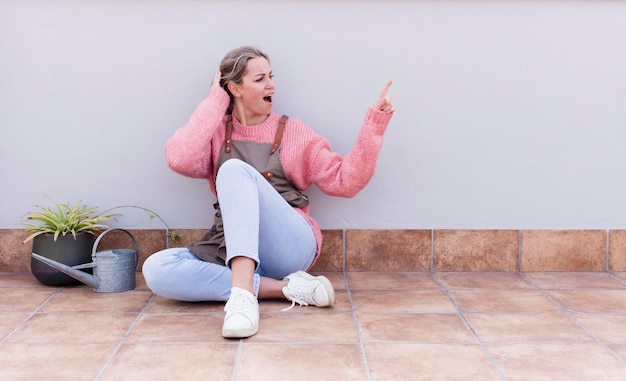 Young pretty blonde gardener woman sitting on the floor with a copy space to the side