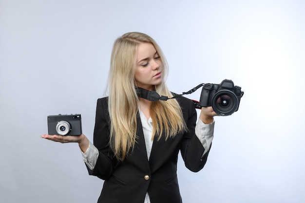 젊고 예쁜 금발 여성은 흰색 바탕에 복고풍 필름 카메라와 현대 DSLR 카메라를 비교한다