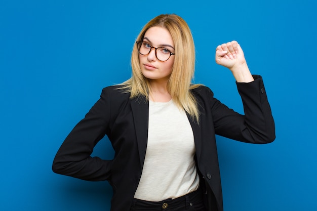 Young pretty blonde woman feeling serious, strong and rebellious, raising fist up, protesting or fighting for revolution