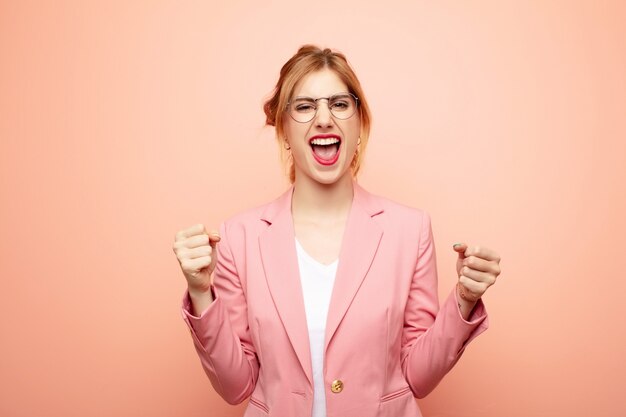 Young pretty blonde woman feeling shocked, excited and happy, laughing and celebrating success, saying wow!