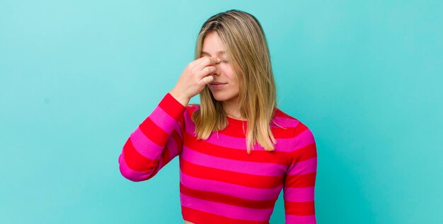 Young pretty blonde woman feeling stressed unhappy and frustrated touching forehead and suffering migraine of severe headache