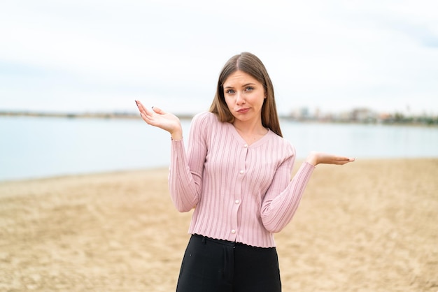 Young pretty blonde woman having doubts while raising hands