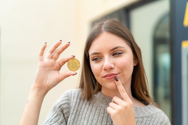 Young pretty blonde woman holding a Bitcoin and thinking