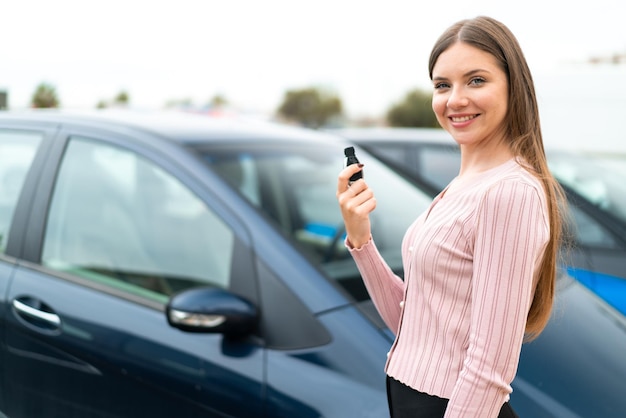 屋外でたくさんの笑顔で車のキーを保持している若いきれいな金髪の女性