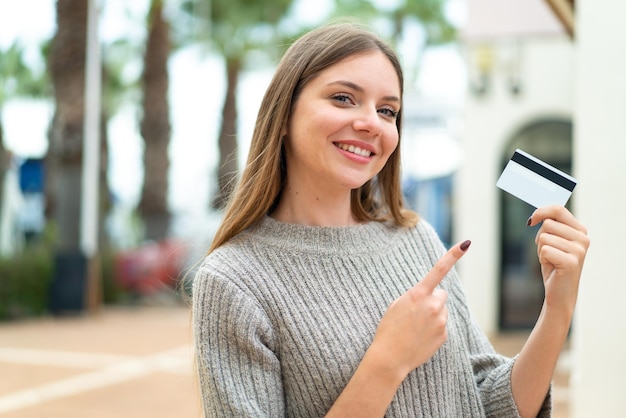 Young pretty blonde woman holding a credit card at outdoors and pointing it