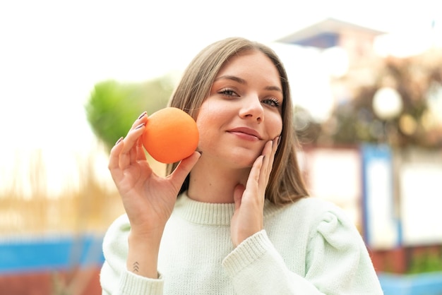 Young pretty blonde woman holding an orange
