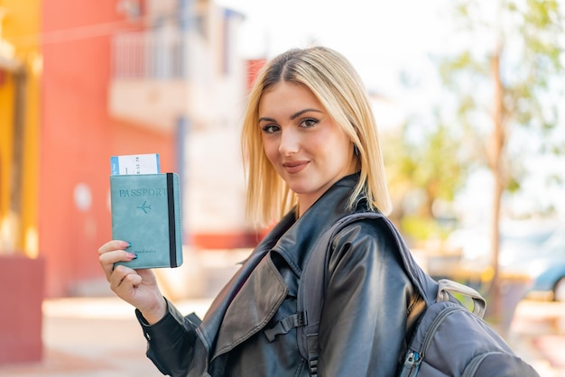 Photo young pretty blonde woman holding a passport at outdoors smiling a lot