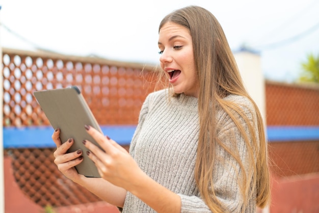 Young pretty blonde woman holding a tablet with surprised expression